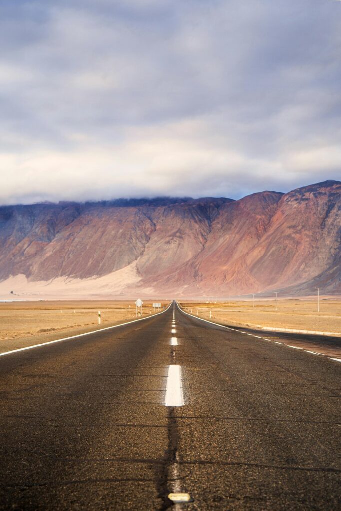 Long highway stretches towards colorful mountains under clouded sky in Iquique, Chile.